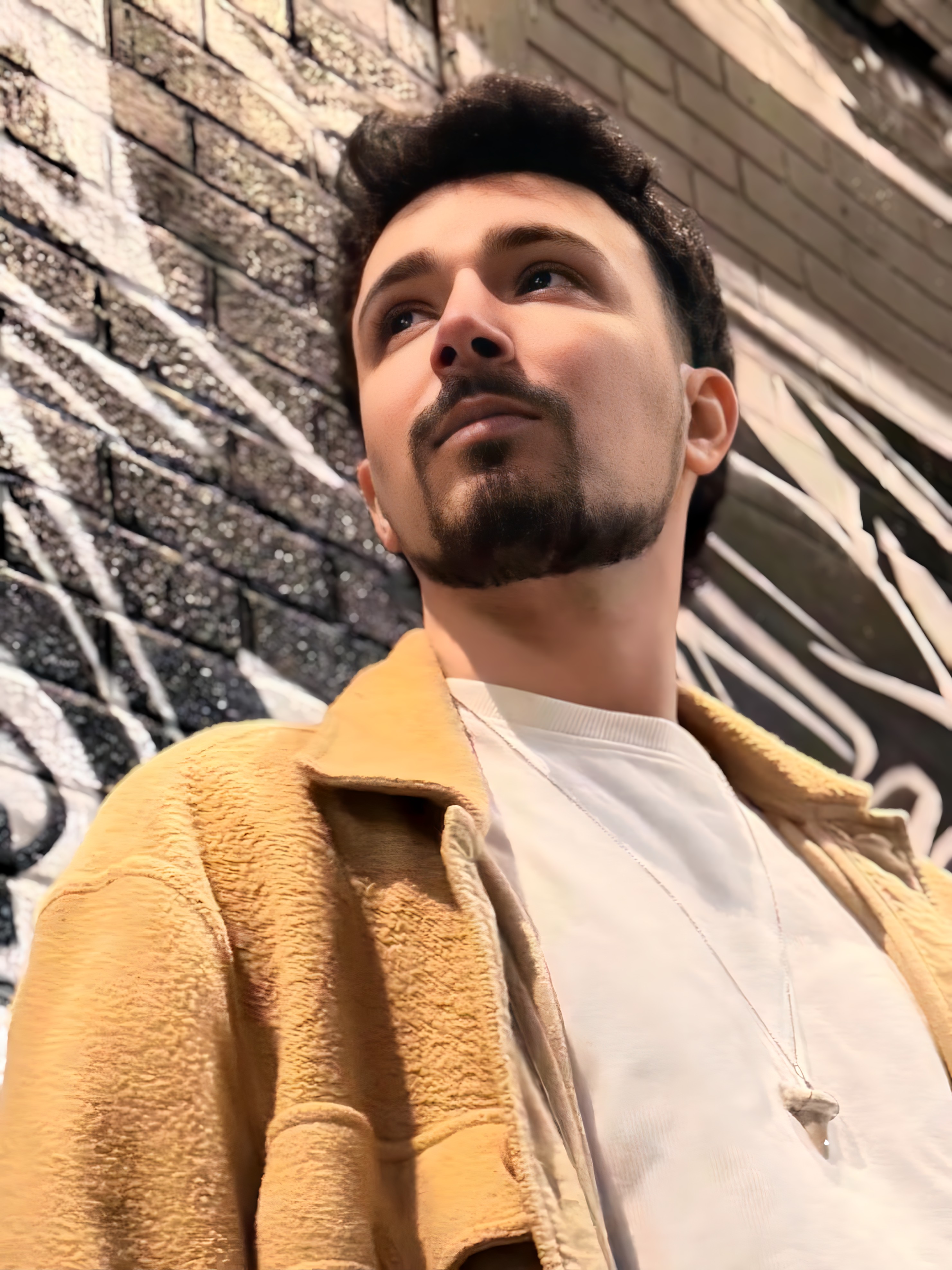WAVEZ outside, looking upward, wearing a brown jacket